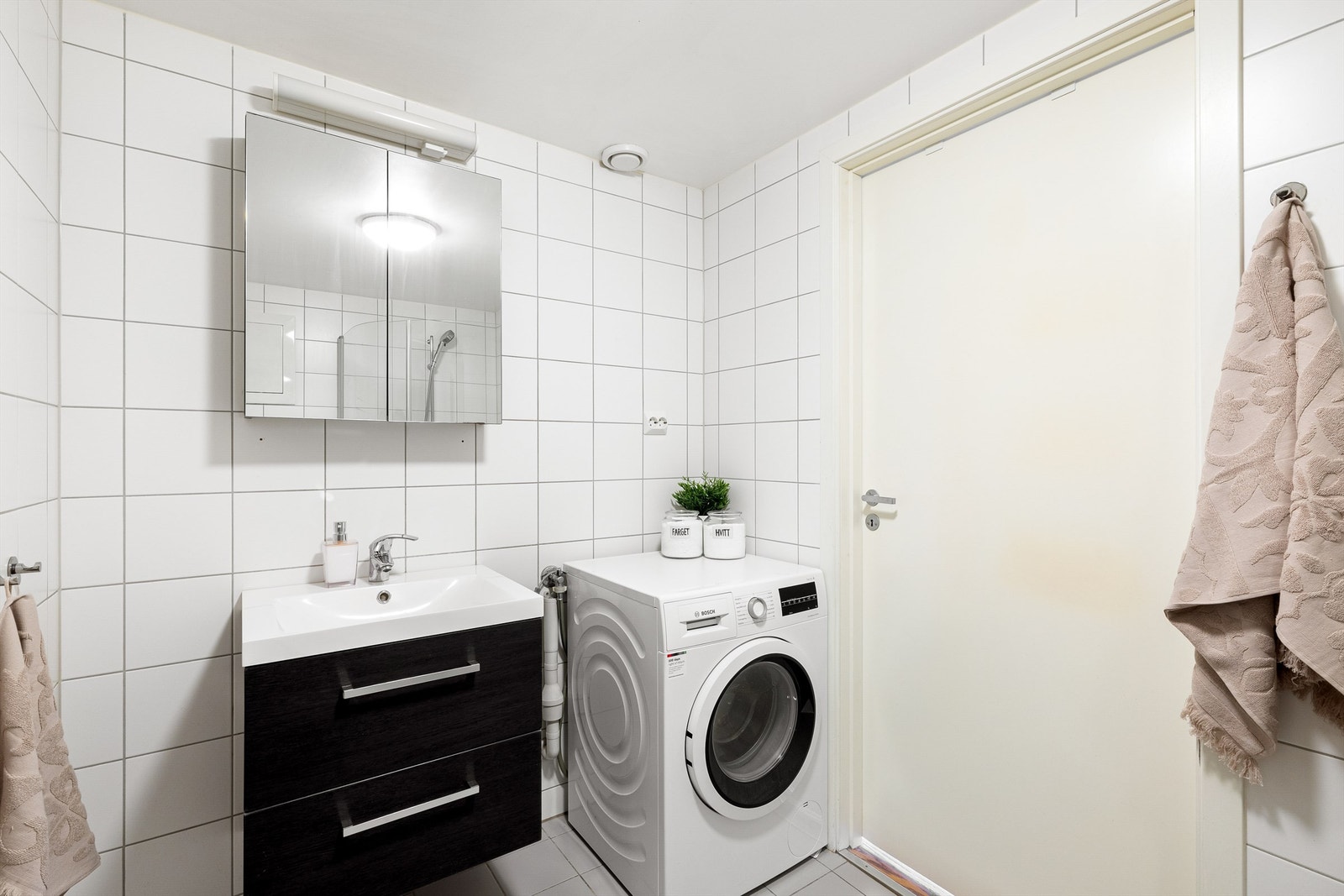 Helfliset baderom med opplegg for vaskemaskin samt moderne baderomsinnredning med god lagring. Galleribilde