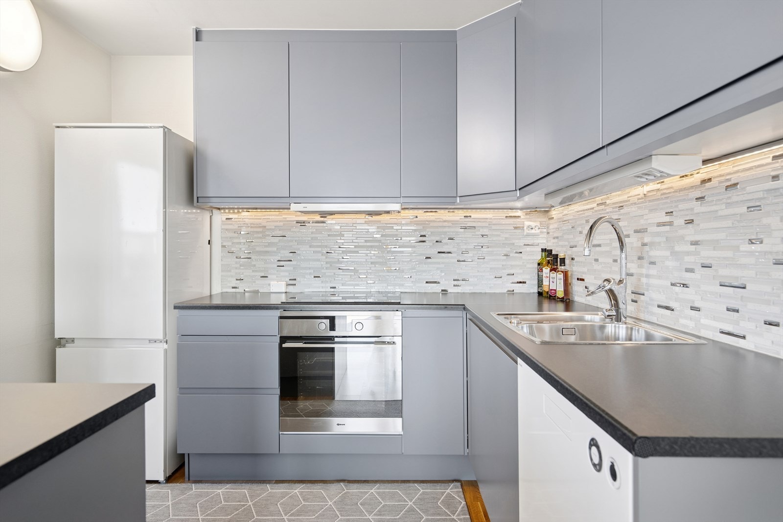 Det er lagt fliser på veggen over benkeplaten, samt belysning under overskapene. Galleribilde