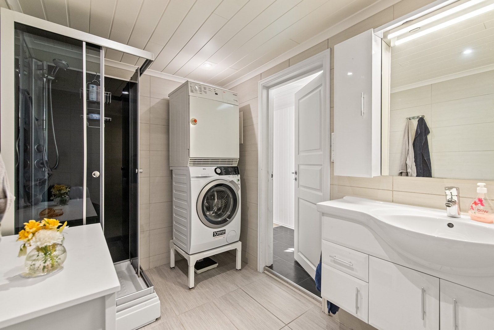 Flislagt bad utstyrt med servant i innredning, dusjkabinett og gulvsatt toalett Galleribilde