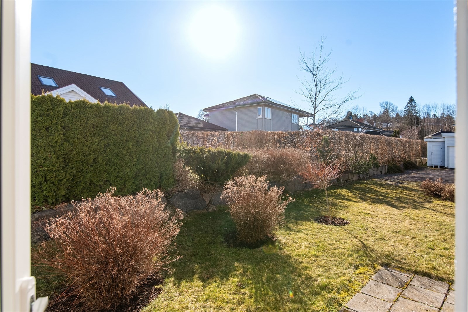 Solrikt grøntområdet med busker, bed og trær. Videre stensatt uteplass på det ene hushjørnet. Galleribilde