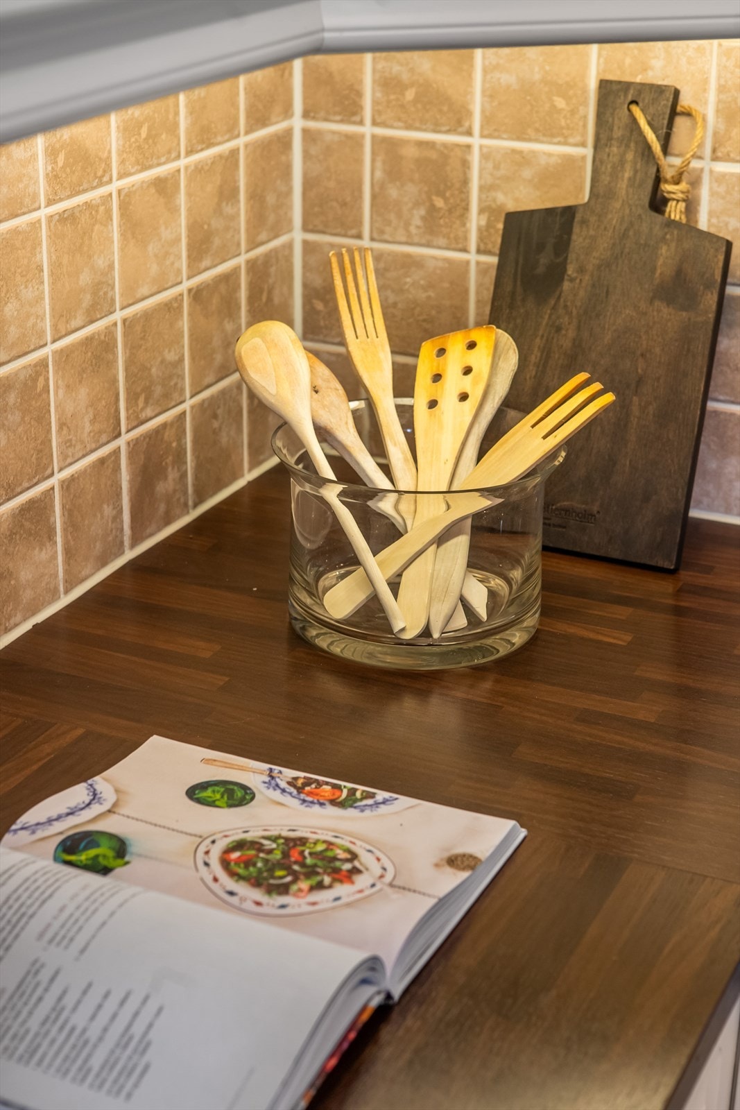 Over benken er det montert grå fliser med dekorfelt, og en ventilator er plassert over kokesonen. Galleribilde