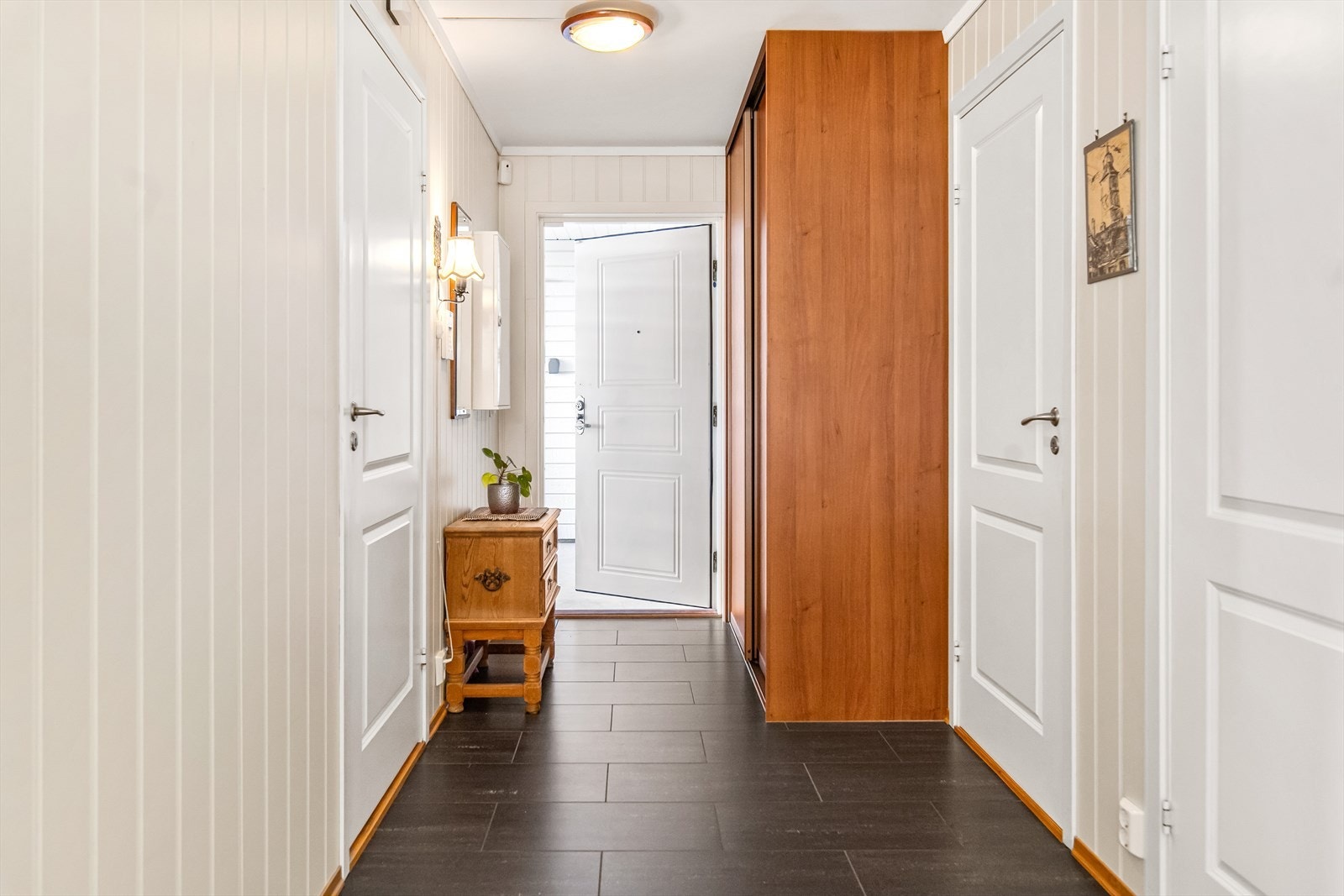 Leiligheten ligger i 1.etasje og har egen inngang via en overbygd ytterdør. Inne ønskes du velkommen av en innbydende entré med sorte fliser på gulvet. Veggene er kledd med lyse panelplater, og varmekabler gir ekstra komfort. Galleribilde