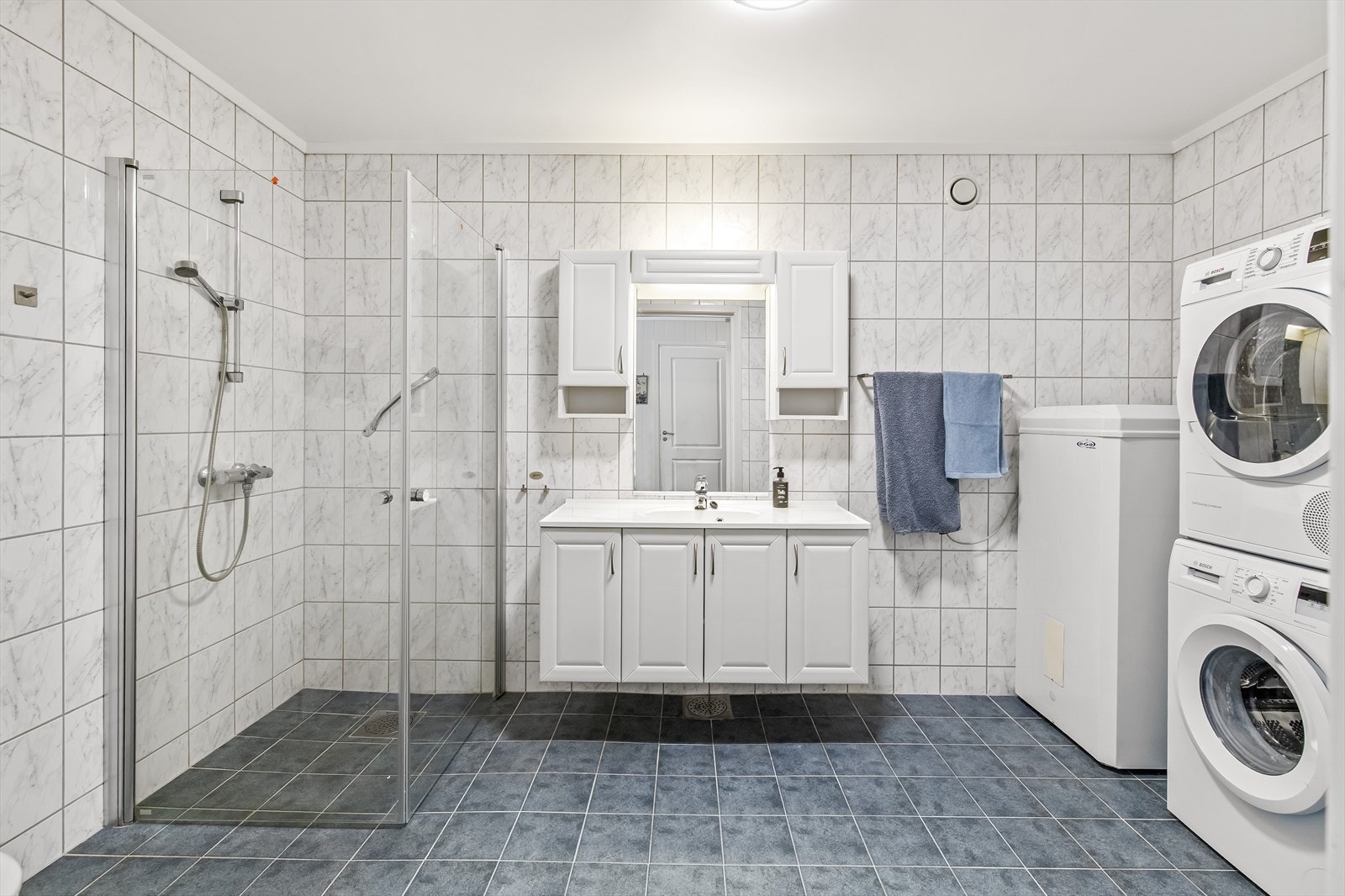 Badet er romslig og har varmekabler for ekstra komfort. Sorte gulvfliser kombineres med hvite veggfliser for et stilrent uttrykk. Galleribilde