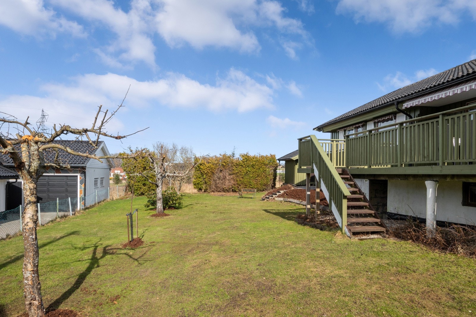 Tomten er pent opparbeidet med trær, bed, busker, flaggstang, stor gressplen og velstelt hekk. Galleribilde