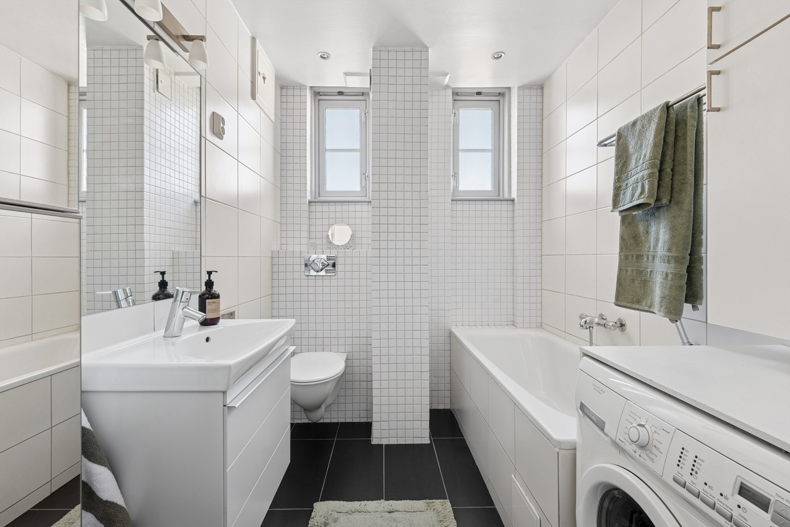 Badet er av god størrelse og har innmurt badekar, dusjhjørne samt opplegg for vaskemaskin og tørketrommel Galleribilde