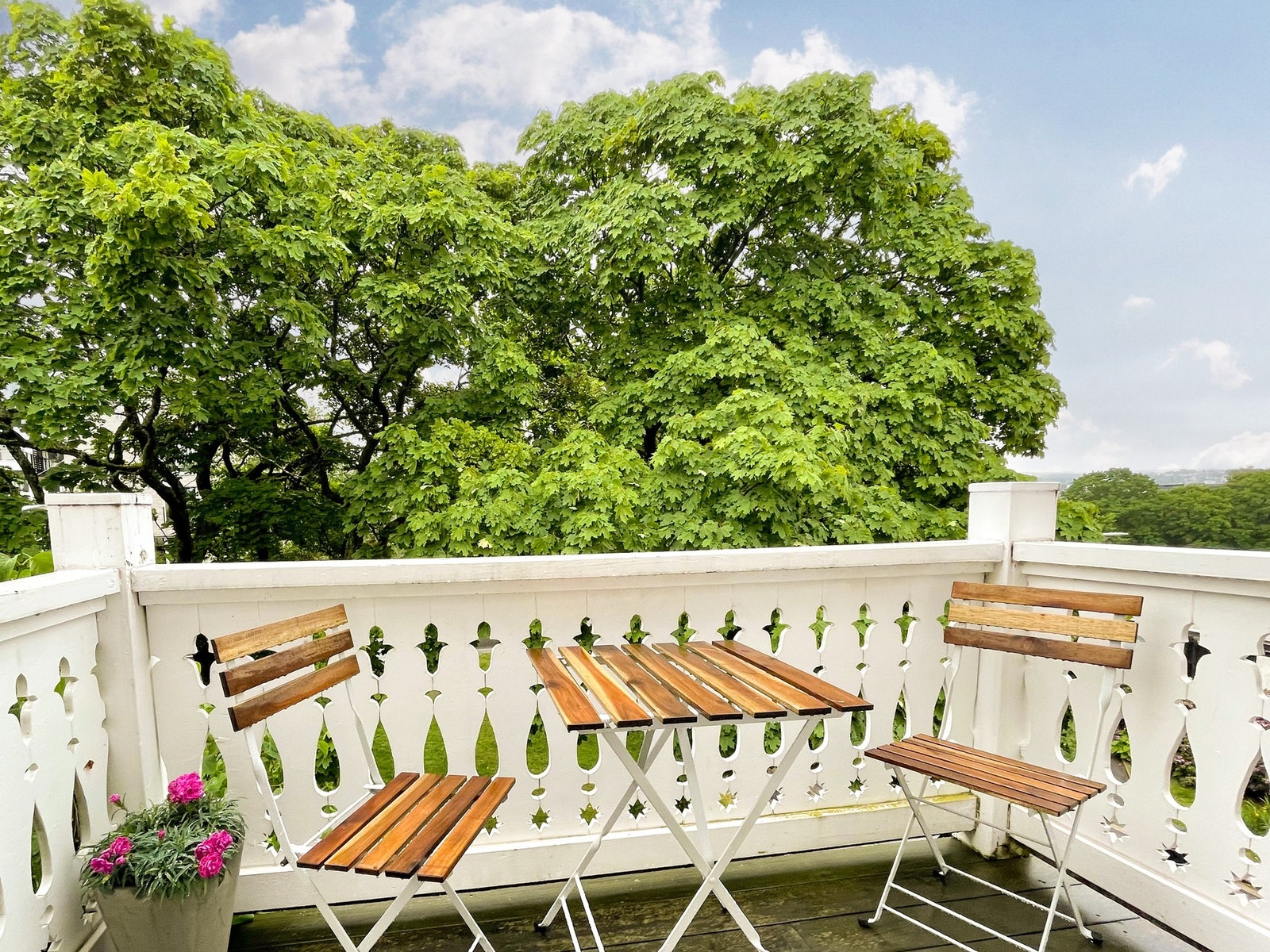Balkongen vender mot en liten park, med morgensol og utsikt til Gamle Aker kirke gjennom løvverket. Galleribilde