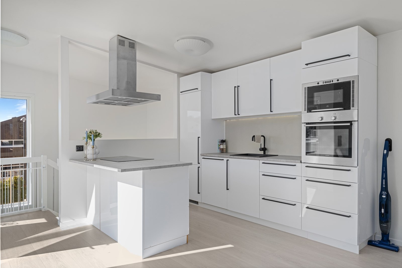 Kjøkkeninnredning med øy og hvite slette fronter og grå benkeplate. Galleribilde