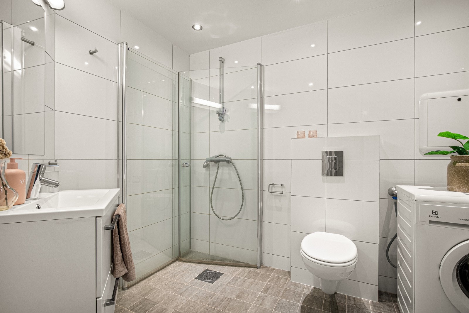 Pent flislagt bad med dusjhjørne, vegghengt toalett og opplegg for vaskemaskin. Galleribilde