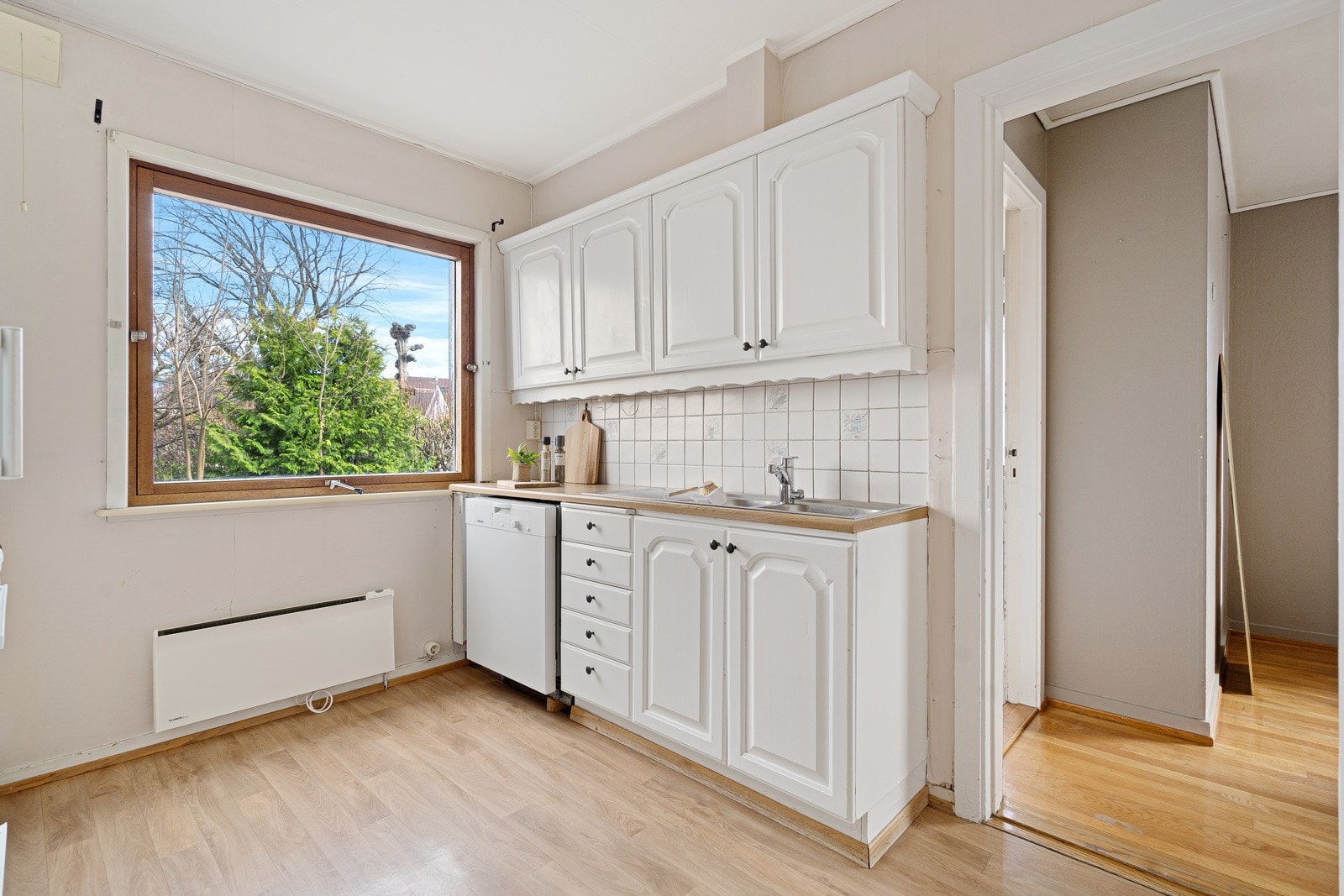 Kjøkkenet har to parallelle benkeskap, med hvite, profilerte fronter, vitrineskap og dobbel oppvaskkum nedfelt i en benkeplate av laminat. Galleribilde