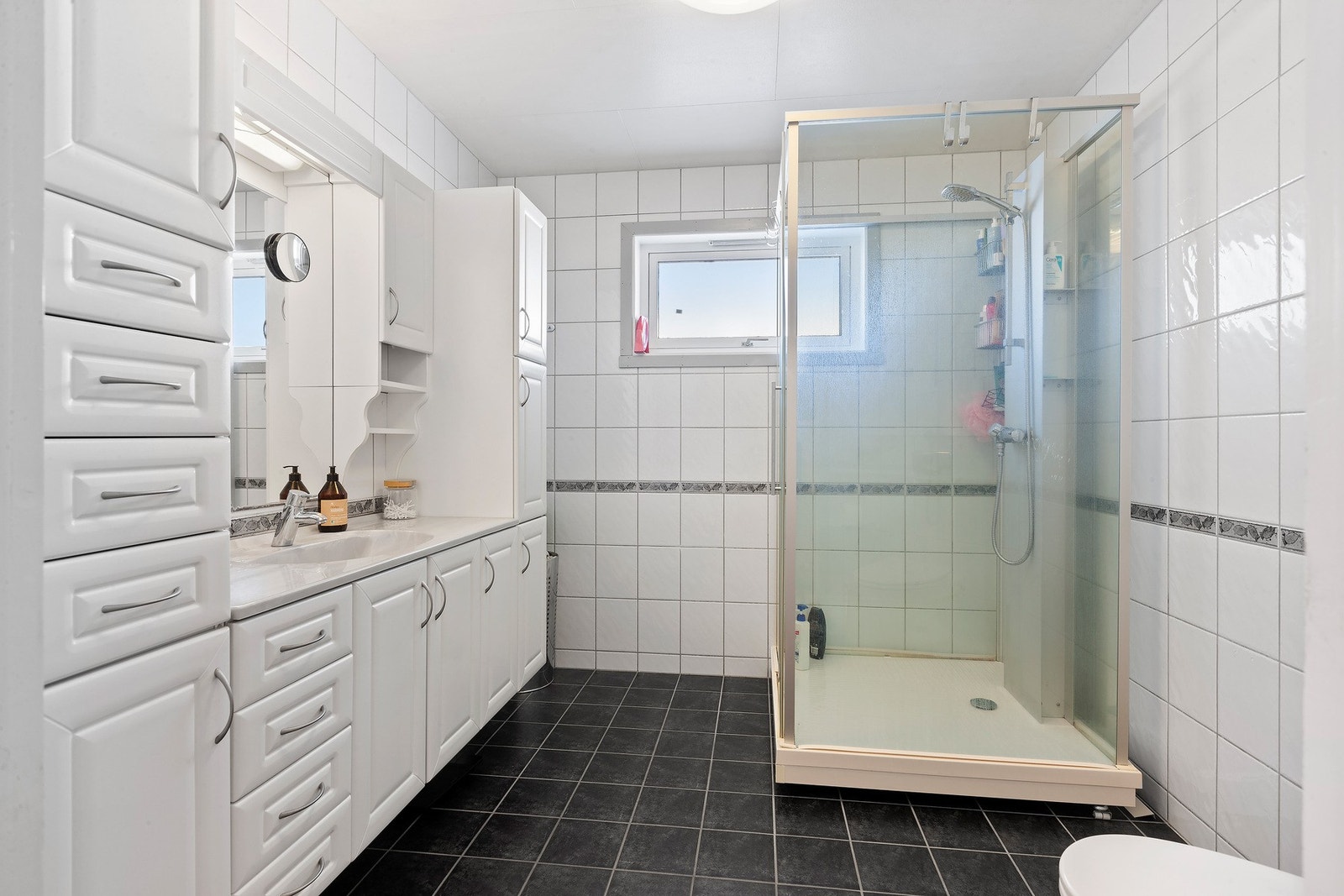 Badet har lys innredning, rikelig med skuffer og skap, dusjkabinett og toalett. Varme i gulv som gir en lun og fin start på dagen. Galleribilde