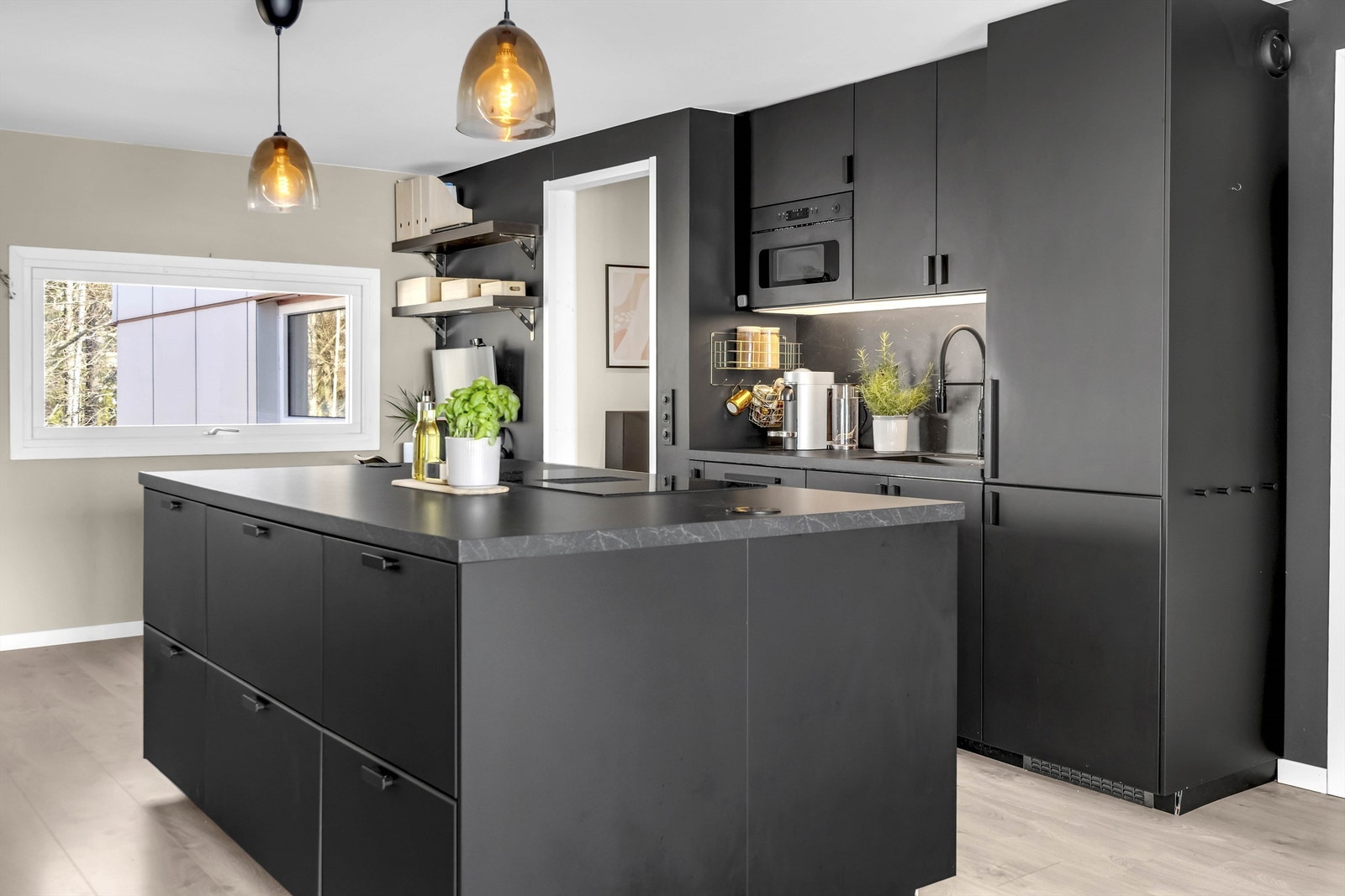 Moderne kjøkkeninnredning med mørke slette fronter og laminat benkeplate med sponkjerne. Ventilator integrert i kokeplate med kullfilter. Kjøleskap, oppvaskmaskin, komfyr og kokeplate. Galleribilde