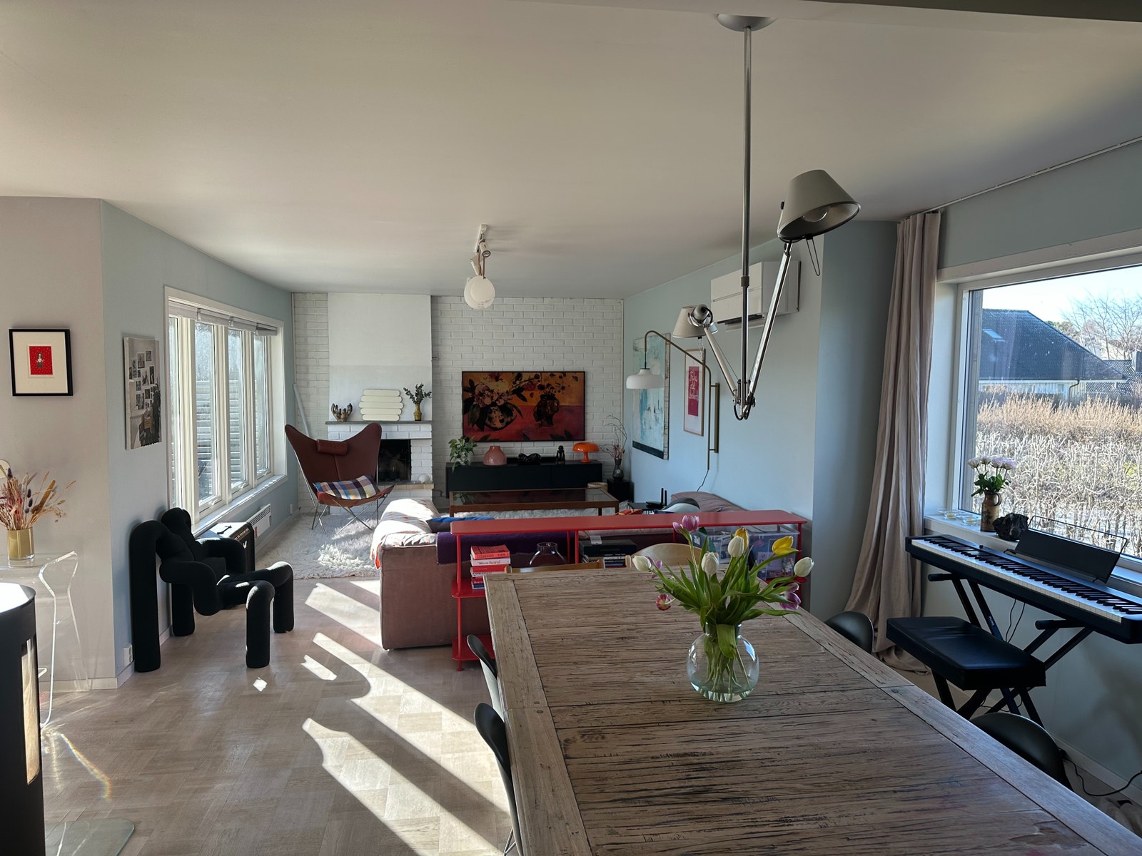 Lys stue med stort spisebord og vinduer ut mot hage og terrasse. Galleribilde