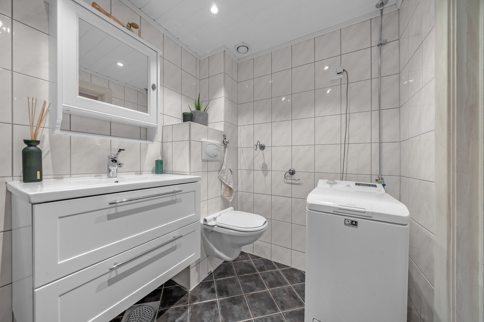 Det inneholder dusjhjørne med innfellbare glassdører, vegghengt toalett, servantskap, speil med belysning og opplegg for vaskemaskin. Det er fellesvaskeri om man vil frigjøre plass på badet. Galleribilde