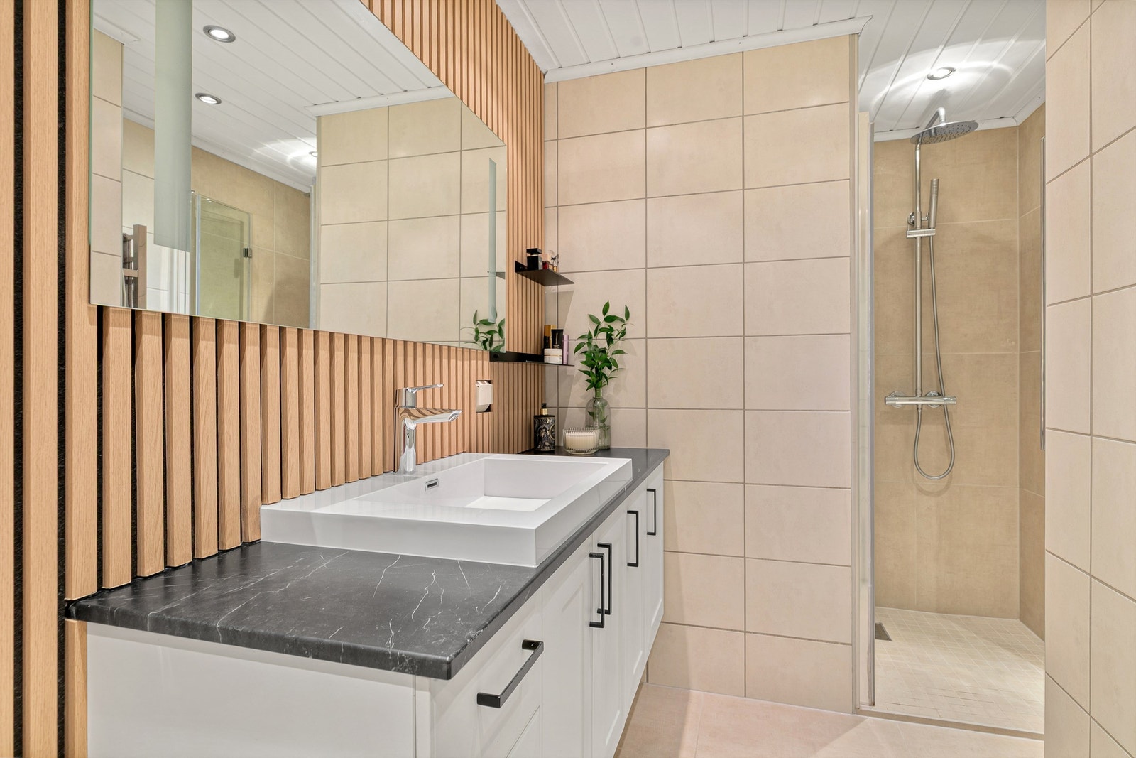 Badet er innredet med beige fliser og en trendy spilevegg for et spennende uttrykk. Galleribilde