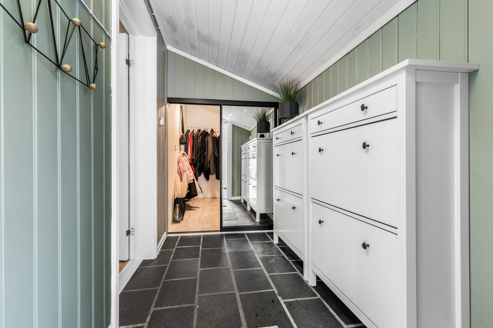 Entreen har sorte gulvfliser med varme. Veggene er kledd med panelplater malt i en dus grønnfarge, og skjult bak skyvedører med speil finner man et praktisk walk-in closet for oppbevaring av yttertøy og diverse utstyr. Galleribilde