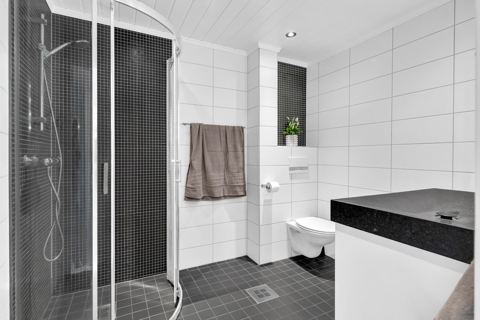 Det moderne badet består av servantskap med 1-greps blandebatteri og underskap. Vegghengt toalett og dusjhjørne med glassdører. Elektrisk gulvvarme. Galleribilde