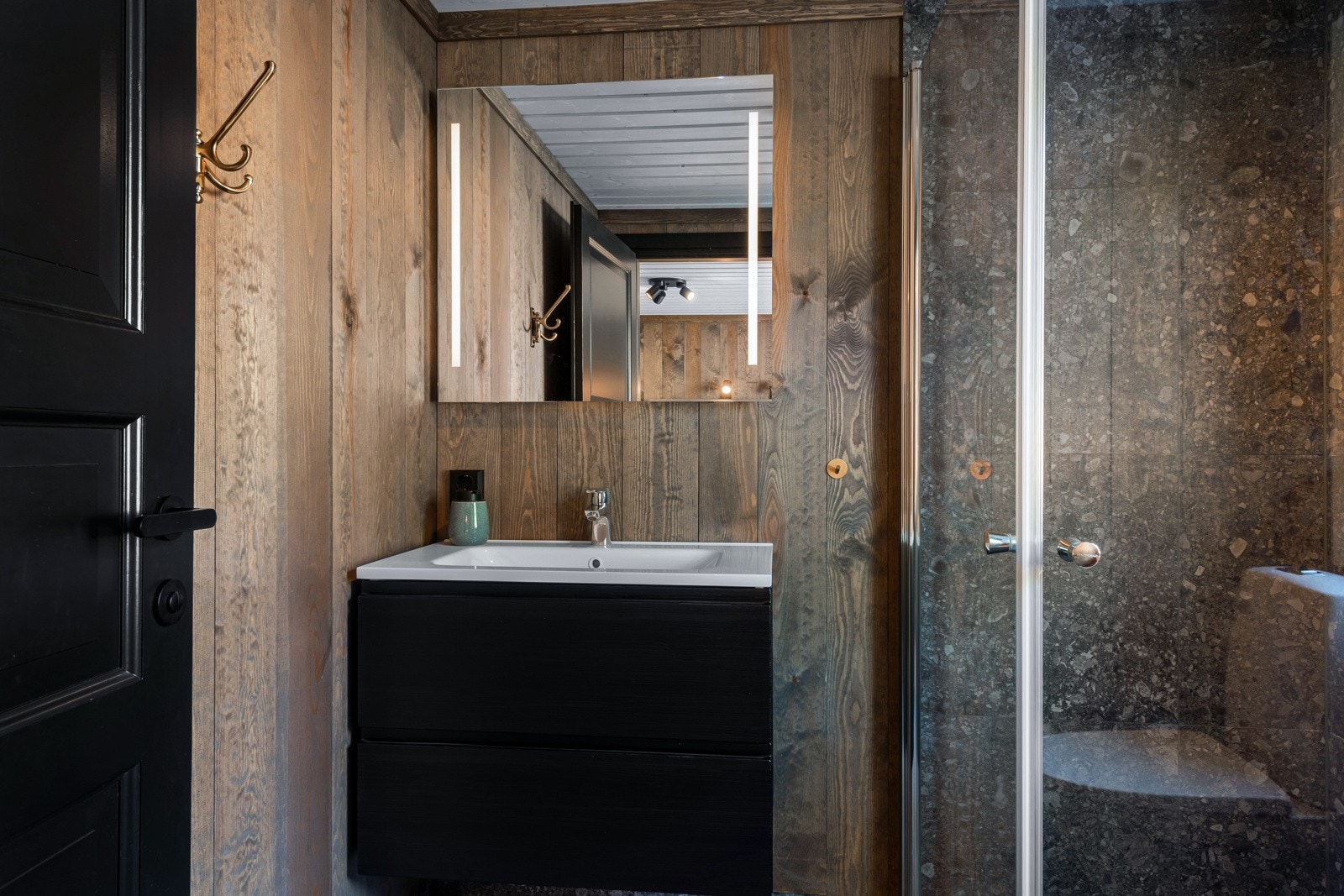 Badet har speil med integrert ledbelysning, heldekkende servant på sort skuffemøblement. Galleribilde