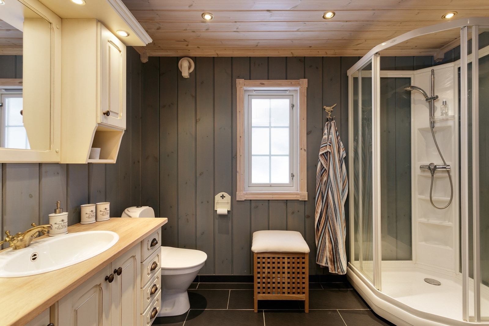 Bad nr. 2 har innredning med profilerte fronter, speil og skap over servant. Gulvstående toalett. Dusjkabinett. Elektrisk styrt vifte. Galleribilde