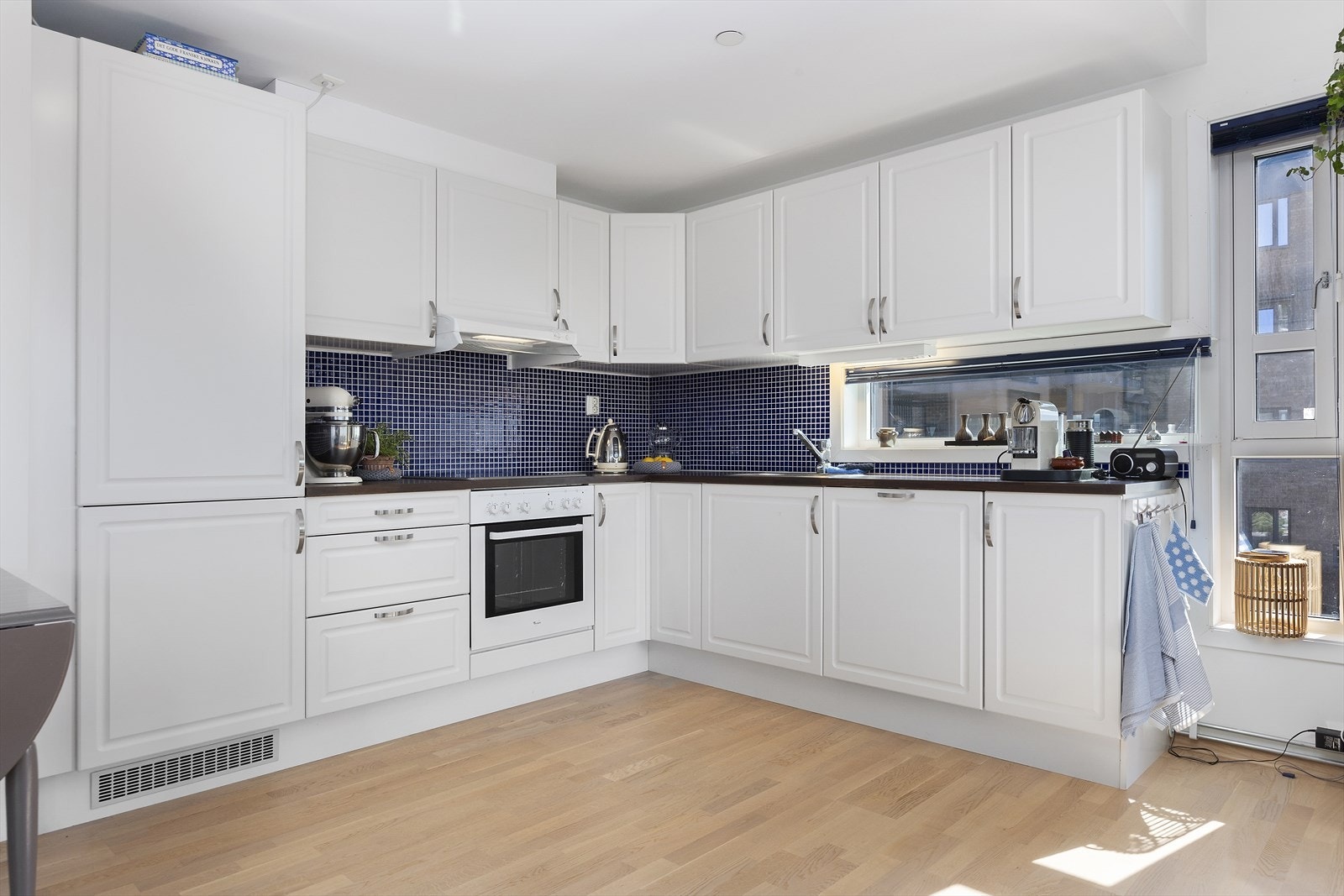 Klassisk kjøkkeninnredning med overflater som består av hvite profilerte fronter og benkeplate av laminat. Galleribilde