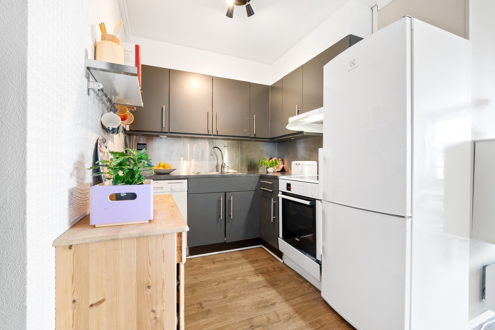 Kjøkkensone delvis avlukket fra stue. Mørk innredning og avtrekk fra komfyrplass Galleribilde