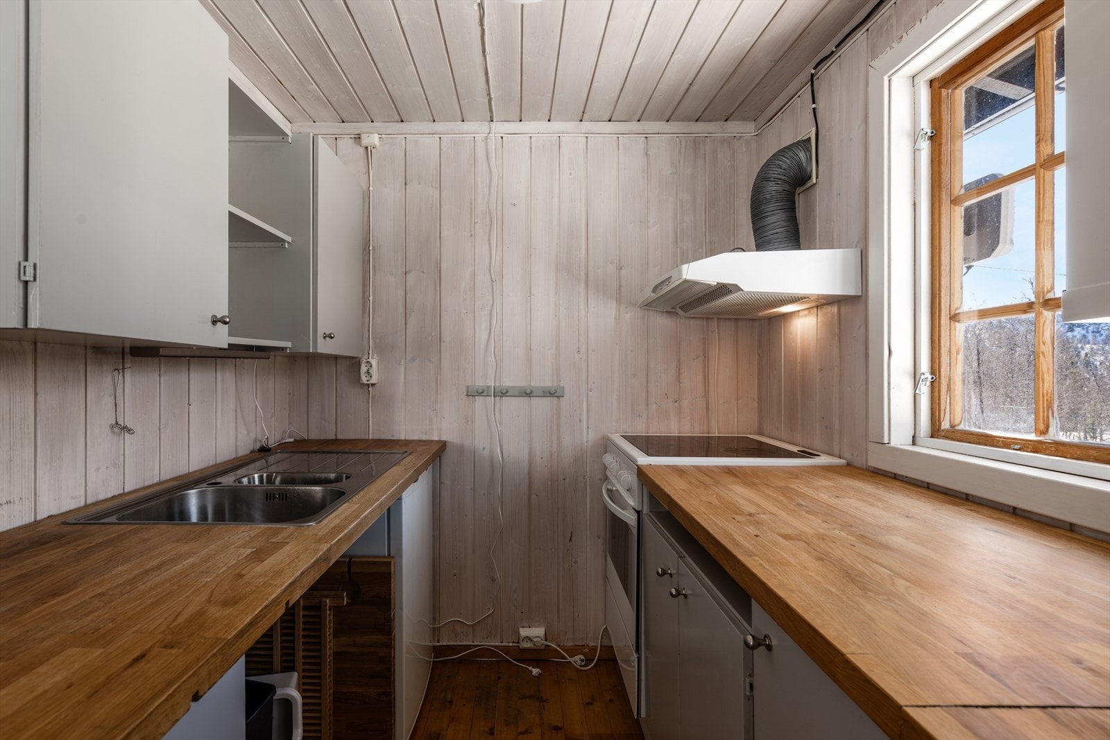 Kjøkken: Lakket tregulv og beiset trepanel på vegger. Kjøkkeninnredning med overskap og underskap, heltre skapdører og heltre benkeplate med oppvaskkum. Komfyr og kjøeskap. Det er kjøkkenventilator med avtrekk ut Galleribilde