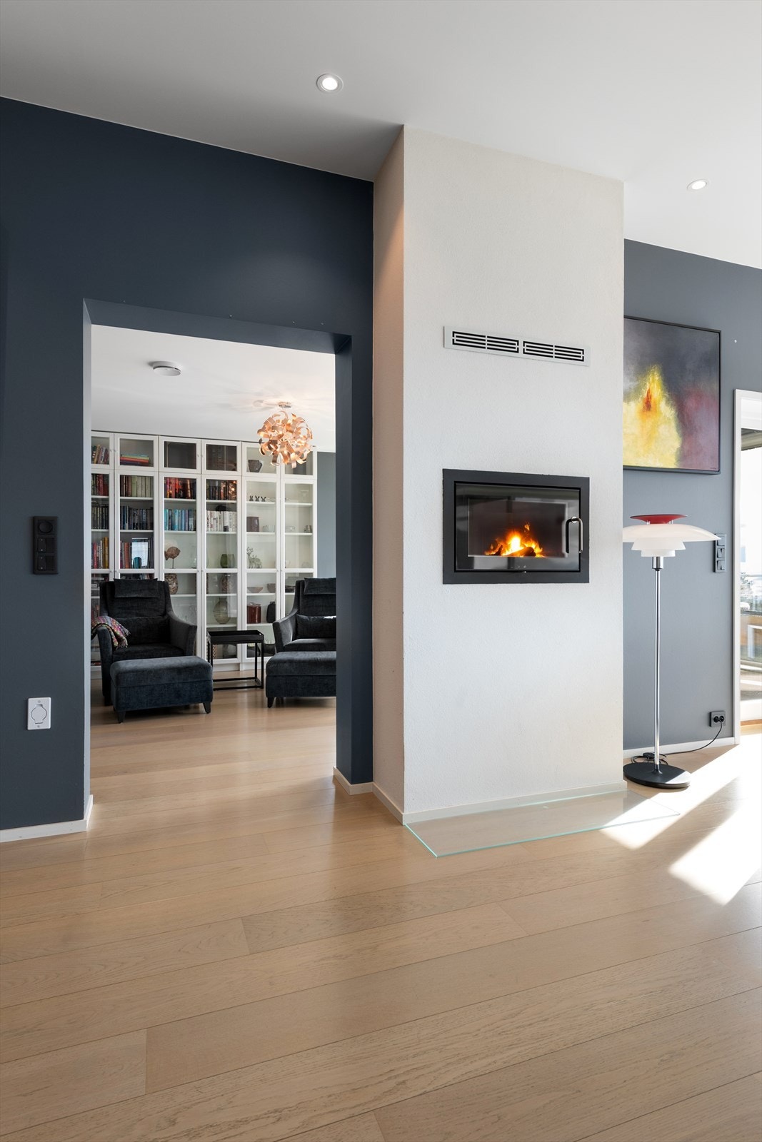 Åpent fra stue mot bibliotek med gjennomgående peis med glassdør på begge sider Galleribilde