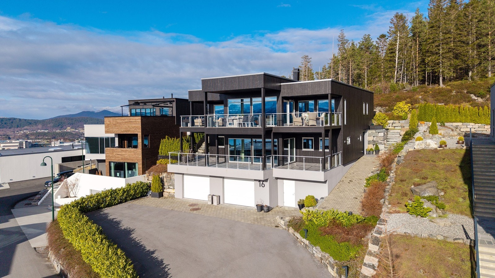 Dronebilde av eiendommen med asfaltert adkomstvei og steinlagte uteområder som er pent opparbeidet og belantet Galleribilde