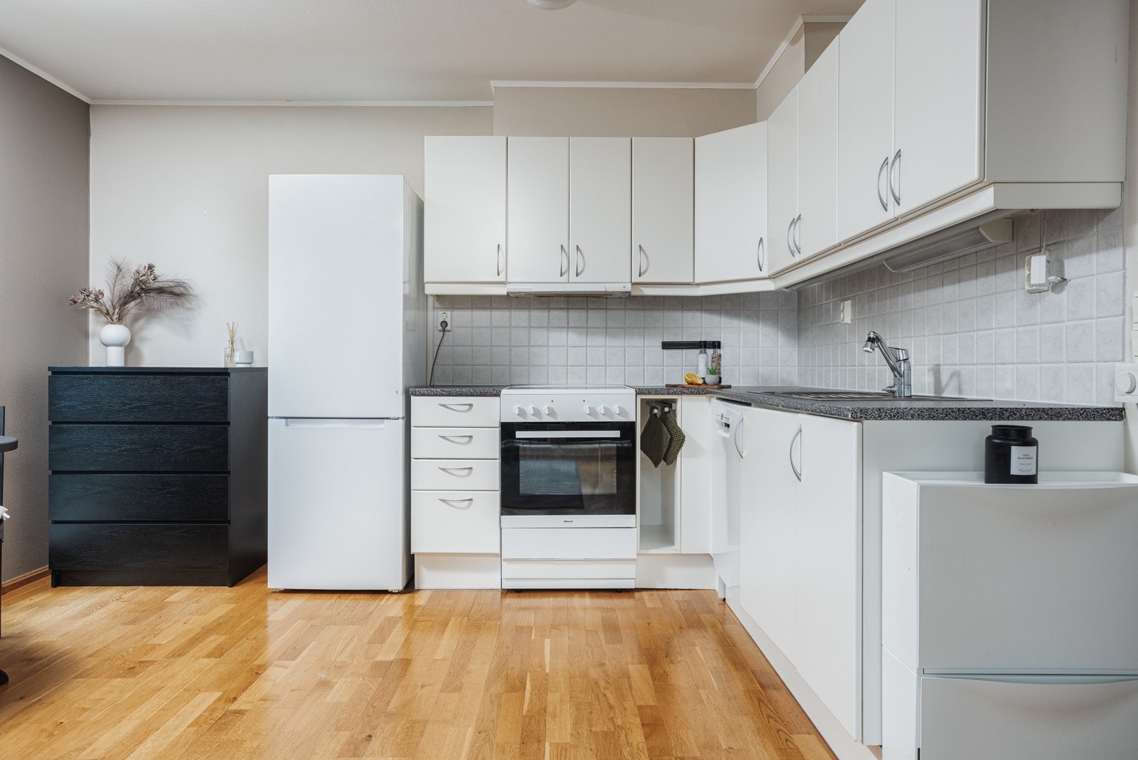 Stuen har en åpen løsning mot kjøkkenet, som er innredet med stilrene hvite fronter og fliser under overskapene - en funksjonell og tidløs kombinasjon Galleribilde