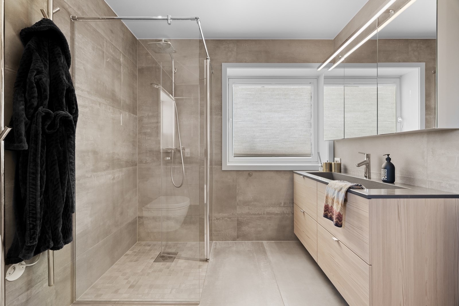 Badet har god størrelse, stilfullt innredet med store, grå vegg- og gulvfliser Galleribilde