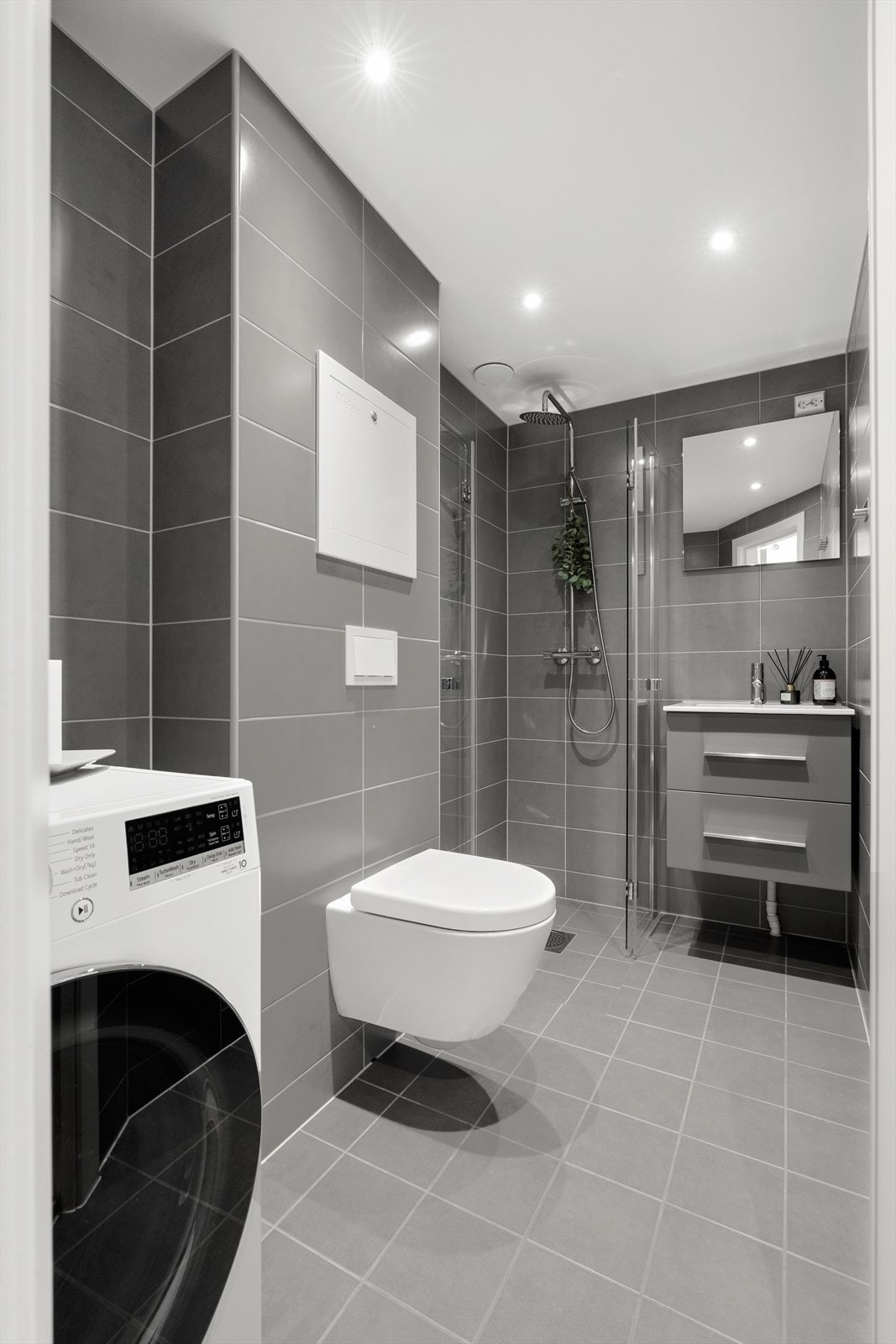 La oss ta en titt på det fine baderommet! Badet er innredet med vegghengt toalett, servant med underskap, dusjhjørne med svingbare glassdører og har opplegg for vaskemaskin. I tillegg er det downlights i himling og varmekabler i gulv. Galleribilde