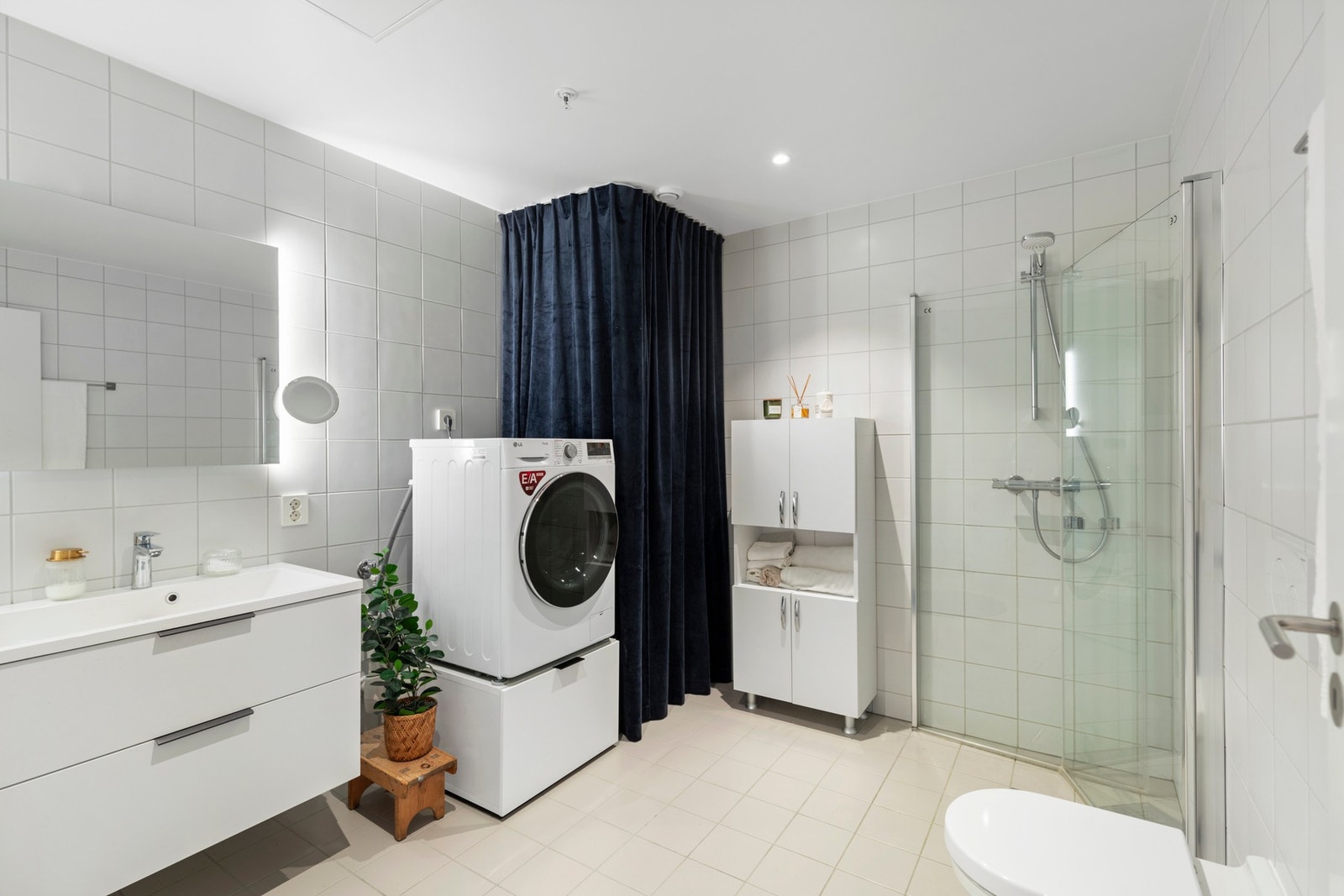 Pent, helfliset bad med tidløse fargevalg. Badet er utstyrt med varme i gulv, spotlights i himling, dusjhjørne med glassdører og vegghengt toalett. Rommet har i tillegg opplegg for vaskemaskin, samt varmtvannsbereder skjult bak forheng. Galleribilde