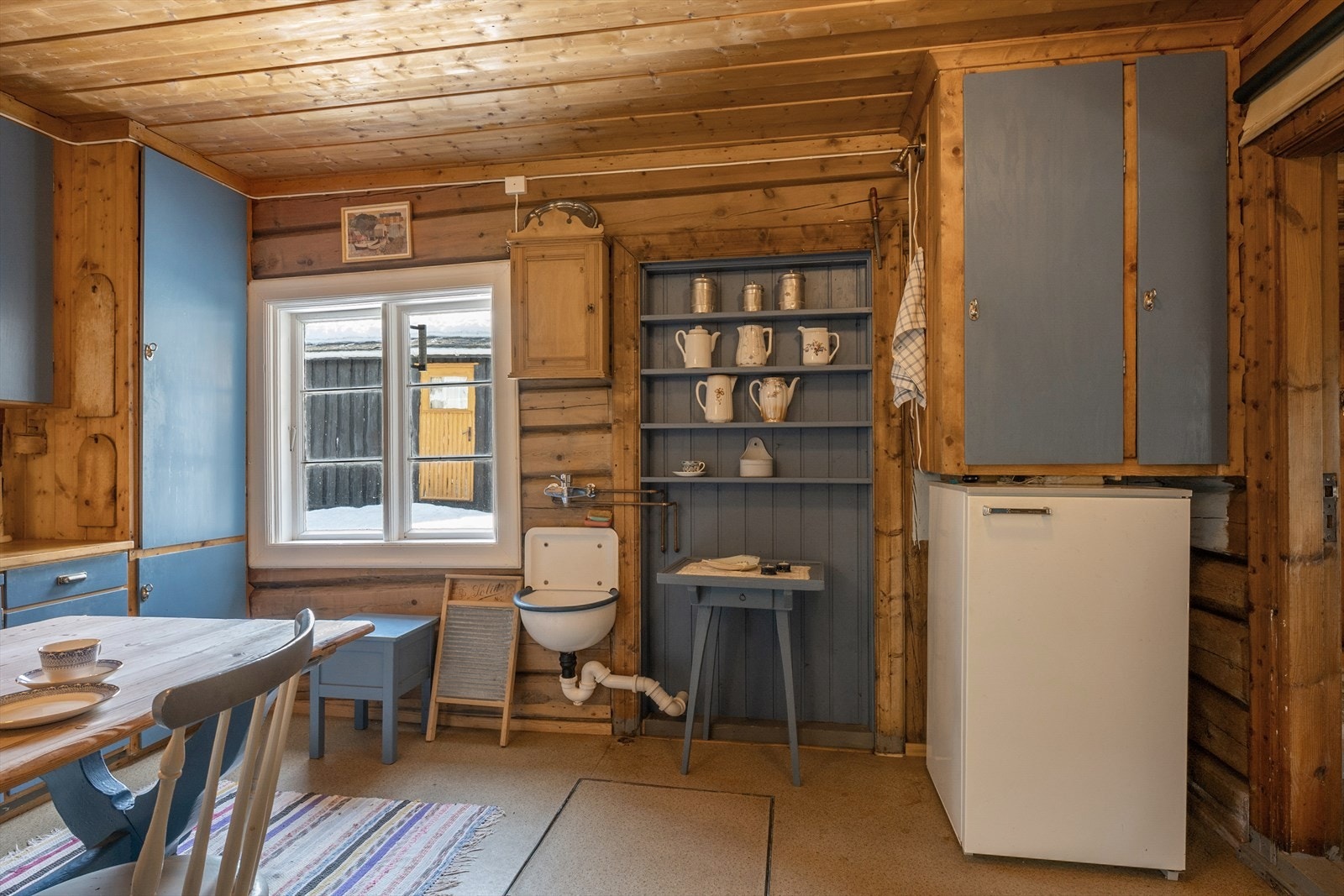 Det er frittstående komfyr og kjøleskap, og vegghengt utslagsvask. I tillegg plass til spisebord. Galleribilde