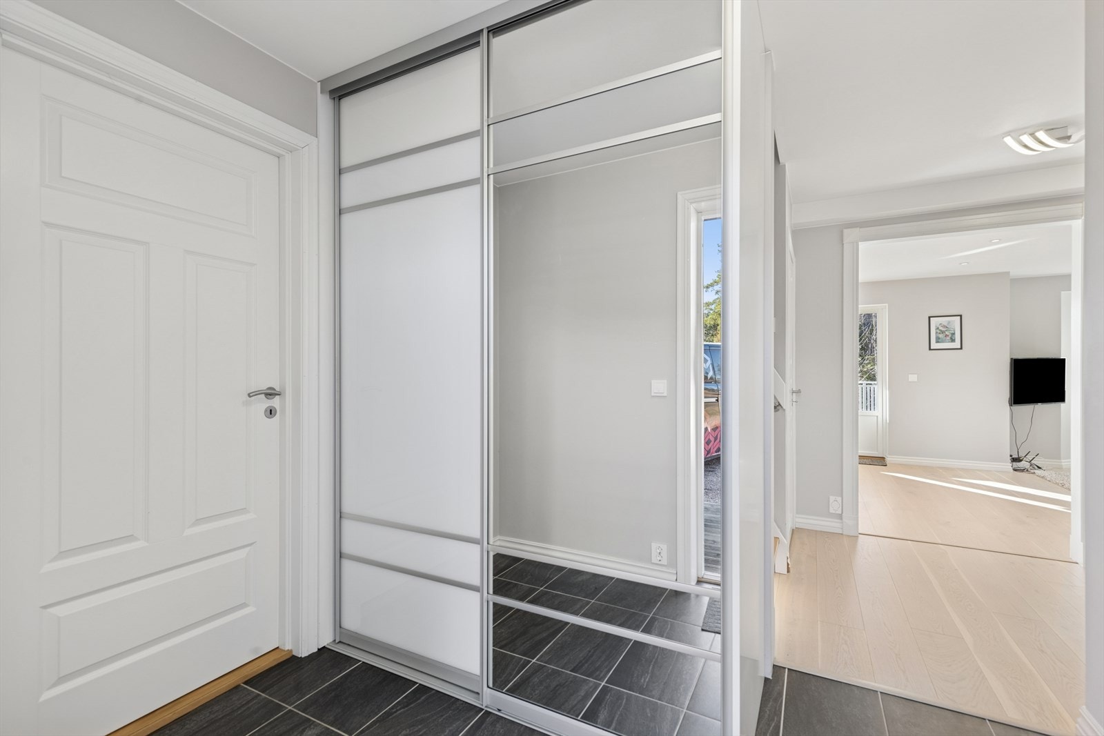 Man ønskes velkommen i en flislagt entré med plass til å henge fra seg yttertøy i skyvedørsgarderobe. Galleribilde