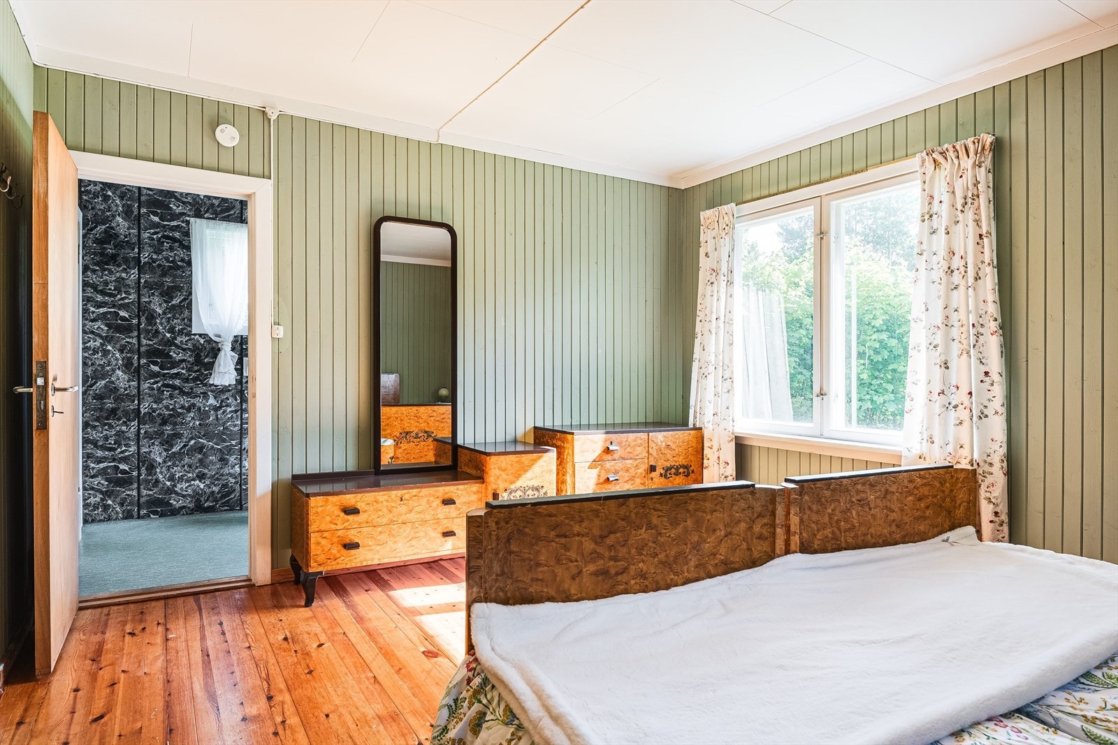 Soverommet har tregulv, panel på veggene malt i en nydelig grønnfarge og vindusflater mot to himmelretninger. Galleribilde