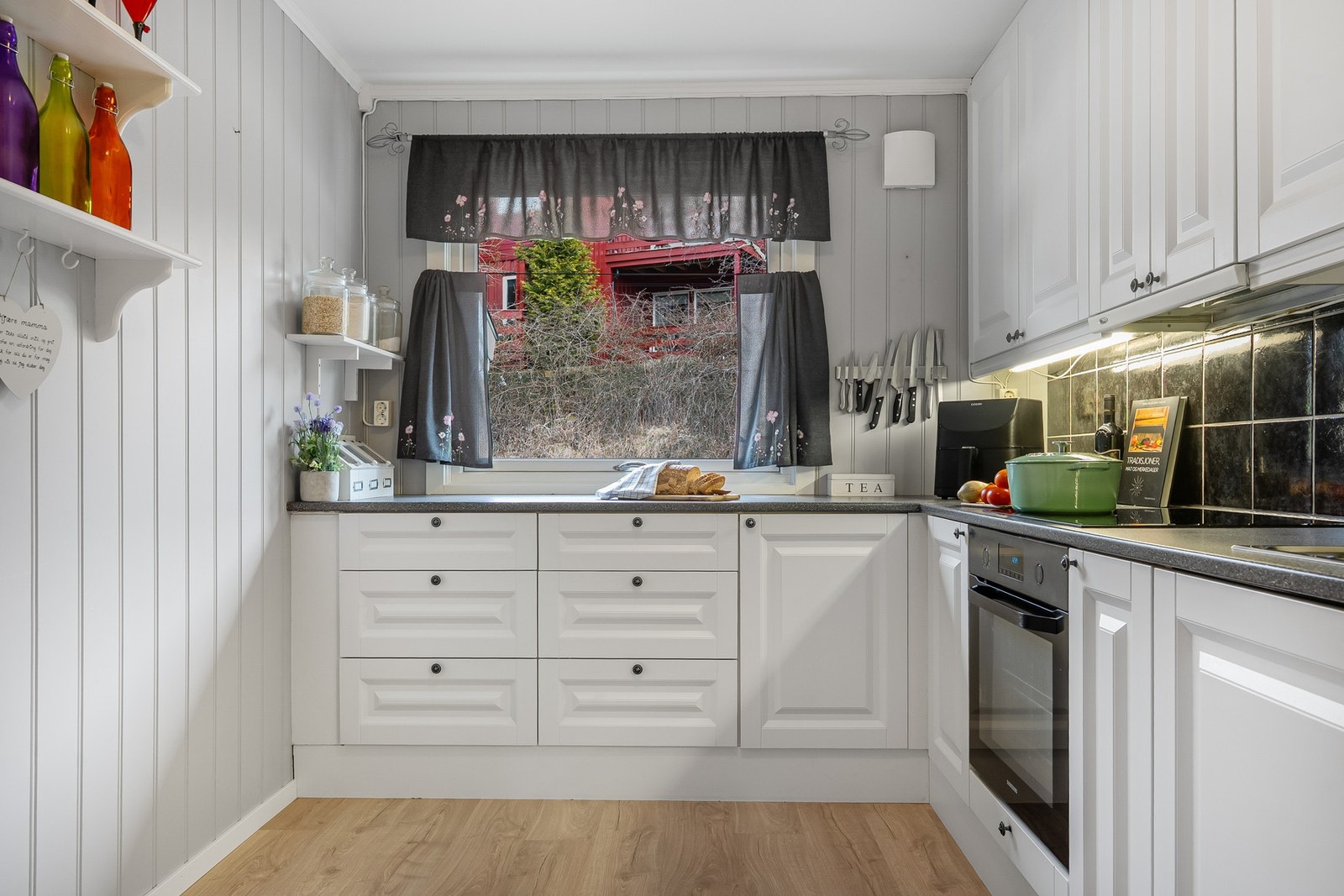 Lys og romslig kjøkkeninnredning med hvite, profilerte fronter og sort laminerte benkeplater. Galleribilde