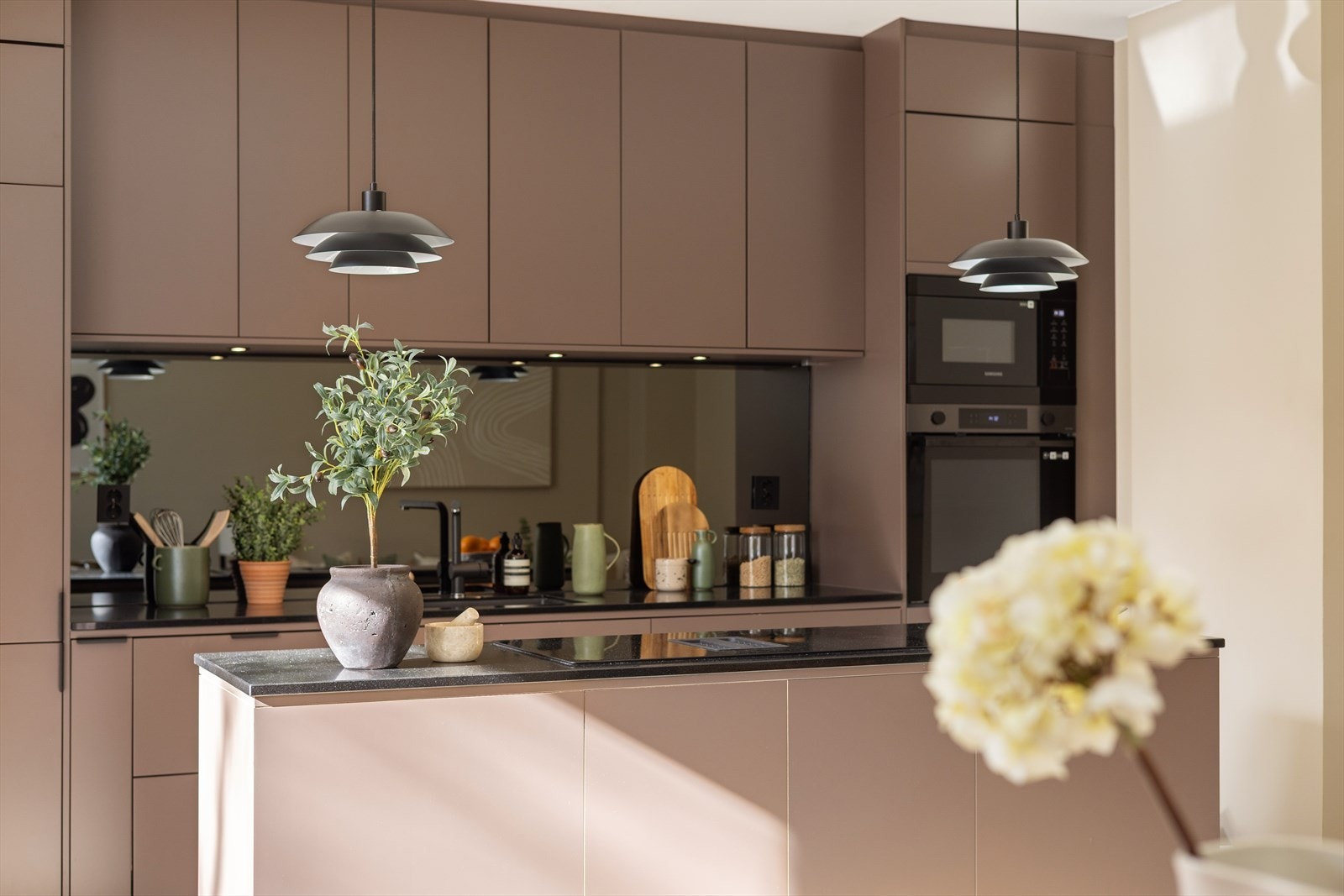 Kjøkkeninnredning med glatte fronter, benkeplaten av stein og speil mellom over og underskap. Galleribilde