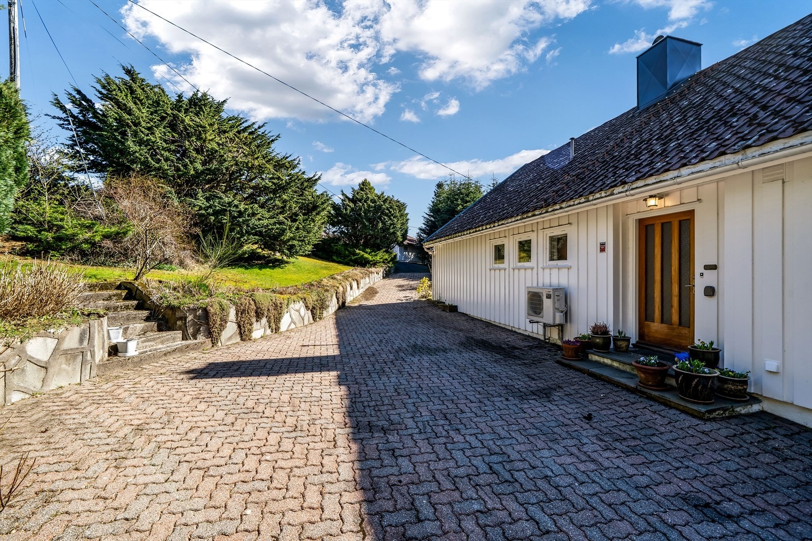 Pent inngangsparti med steinsatt uteområde og beplantning i skråning. Galleribilde