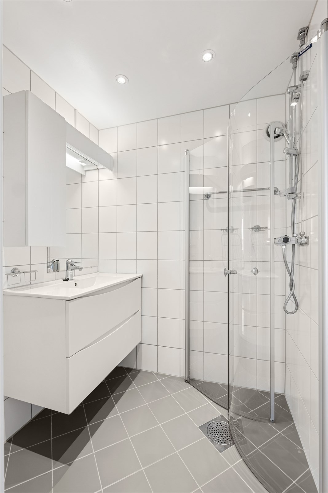 Badet er både lyst og pent, utført med en moderne servantinnredning, overskap, speil og dusjhjørne. Det er god belysning over speil og via spotter i tak. Galleribilde