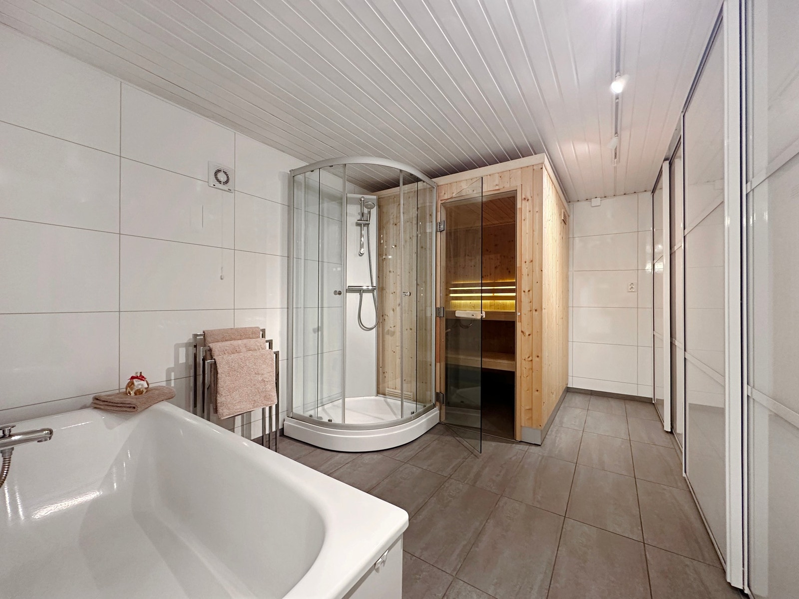 Baderom i underetasjen fra 2014. Her er det bl.a. badekar, dusjkabinett og badstue med belysning. Langs hele veggen til høyre i bilde er det en stor "skreddersydd" skyvedørsgarderobe. Galleribilde