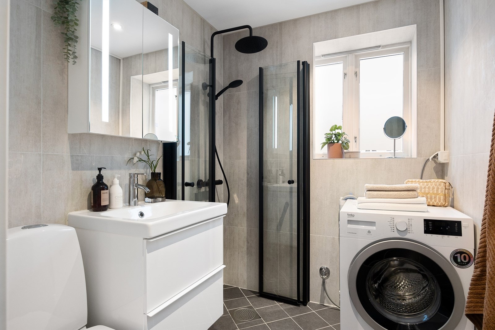 Stilrent, flislagt baderom med gulvvarme. Rommet har servant, gulvstående toalett og dusjhjørne med innfellbare glassdører. Galleribilde