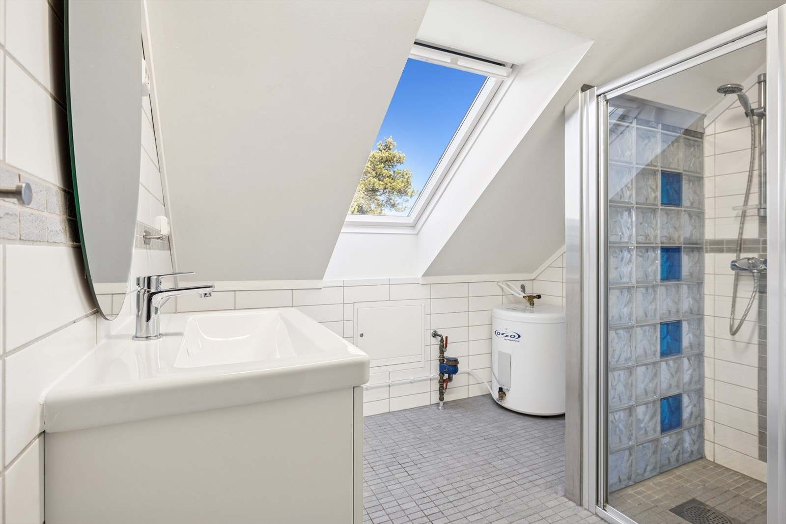 Badet er tidløst innredet med en kombinasjon av grå og hvite fliser. Badet er i dag utstyrt med dusjhjørne, vegghengt toalett og servant med skuffer. Galleribilde