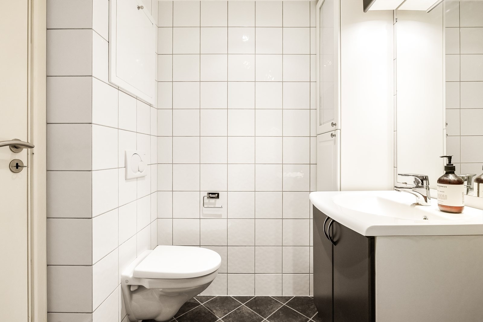 Badet er utstyrt med vegghengt toalett, dusj, servant med oppbevaringsplass og opplegg for vaskemaskin og tørketrommel Galleribilde