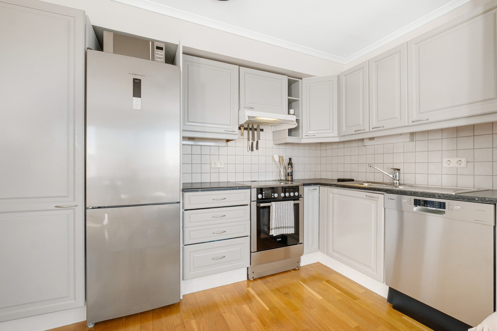 Stilrent kjøkken med lyse fronter og fliser over benkeplaten Galleribilde