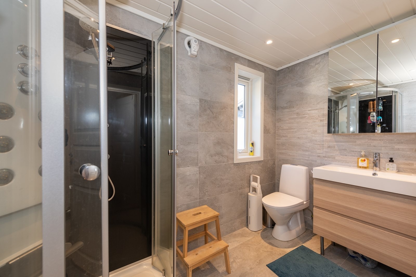 Badet har flislagt gulv og vegger. Badet inneholder enkelt servant, klosett og dusjkabinett. Galleribilde
