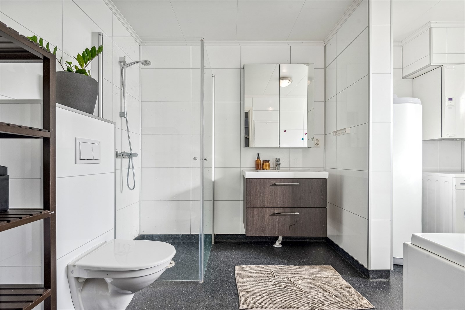 Moderne baderomsinnredning med skuffer og heldekkende servant, stort speilskap over. Praktisk med plass og opplegg for vaskemaskin bak delevegg. Galleribilde