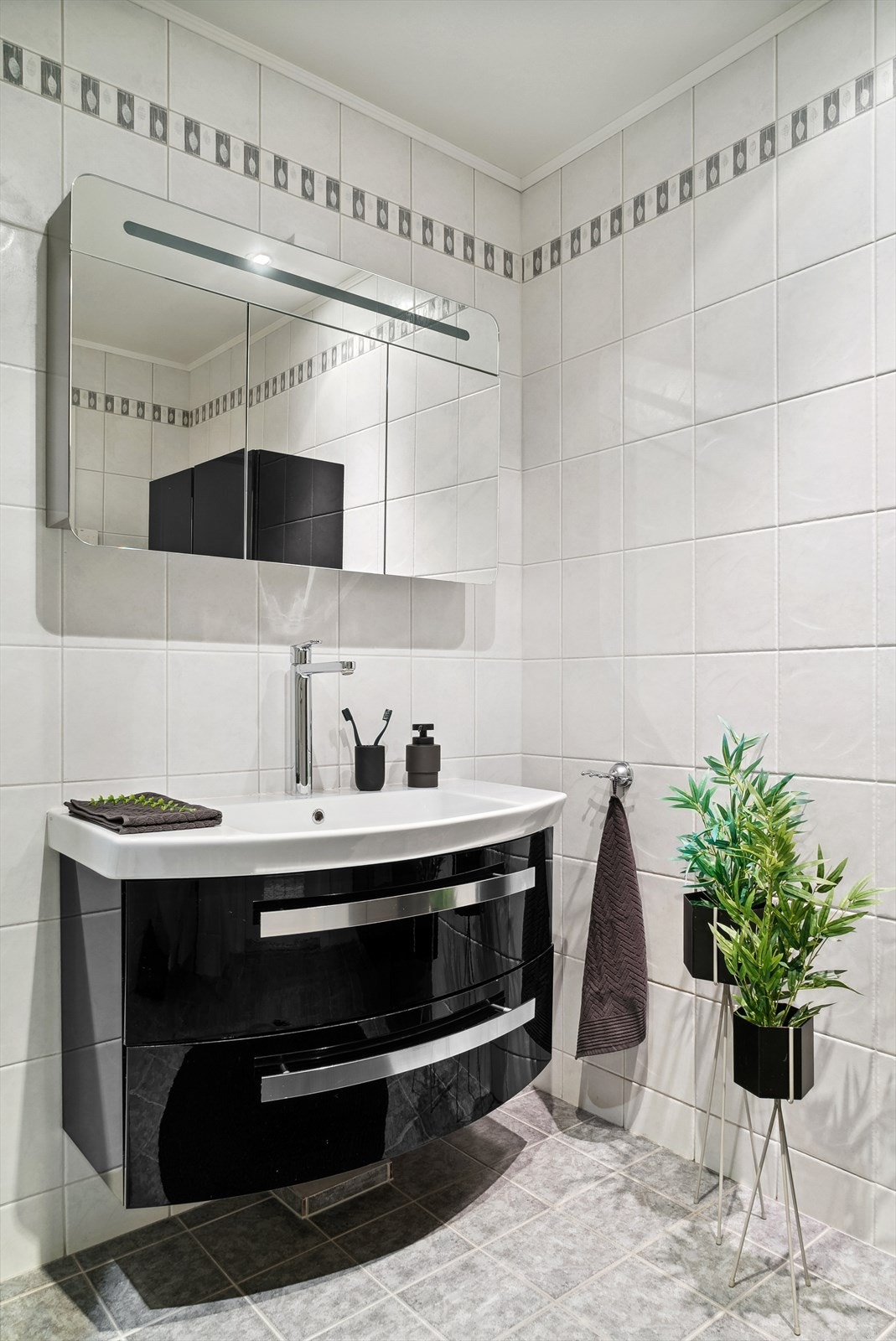 Sort baderomsinnredning med 2 skuffer og servant med høyt blandebatteri. I rommet er det også veggmontert toalett, dusjkabinett og godt med skapplass. Galleribilde