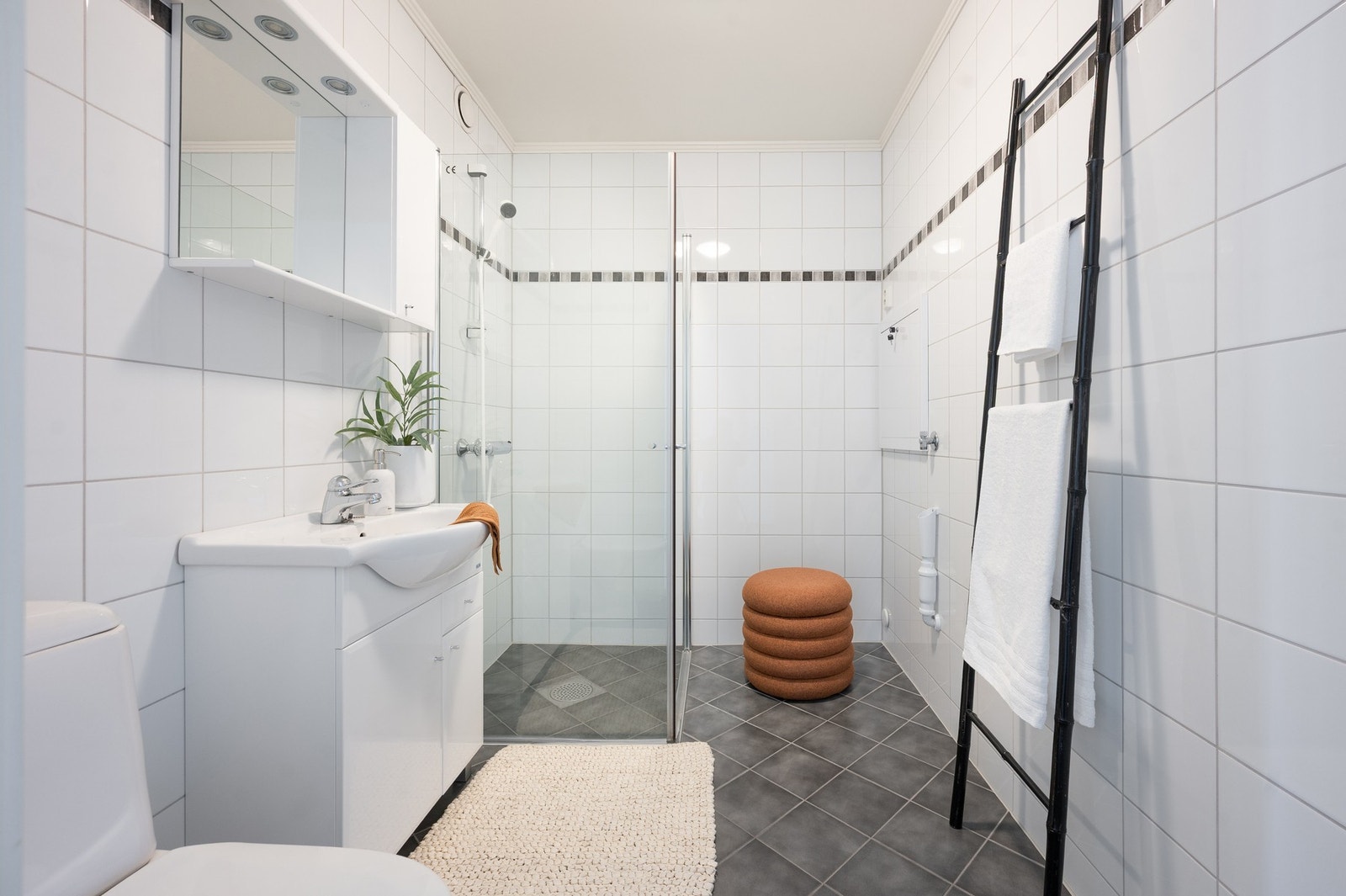 Badet er innredet med speilinnredning med belysning. servant, dusjhjørne med innfellbare glassdører, gulvstående toalett og opplegg for vaskemaskin. Galleribilde