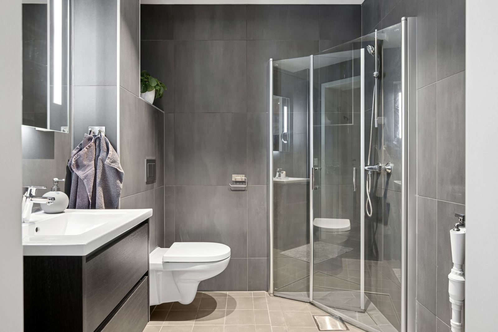 Badet i underetasjen er moderne og stilfult med store mørke fliser, dusjhjørne og vegghengt servantskap. Galleribilde