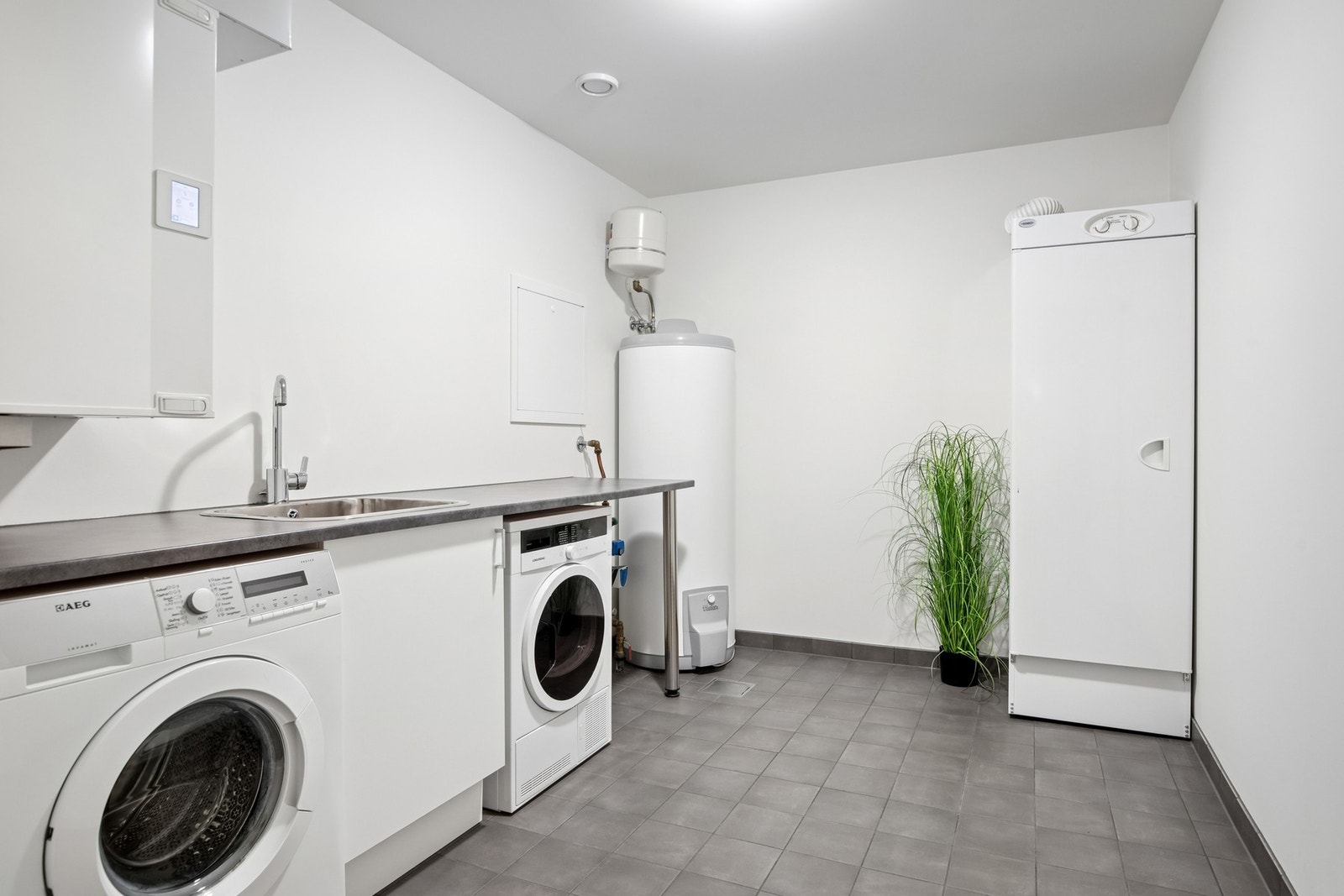Vaskerom med praktisk utslagsvask og benkeplass samt opplegg for vaskemaskin og tørketrommel. Galleribilde