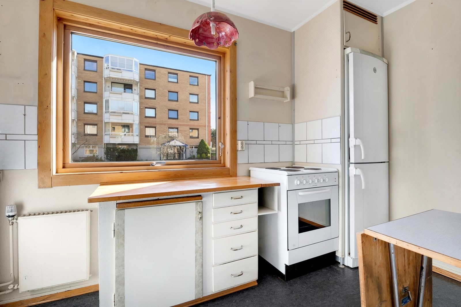 Kjøkken med belegg på gulv, malte vegger og malt tak. Original kjøkkeninnredning med malte slette fronter, heltre benkeplate med fliser over og dobbel oppvaskkum med helt benkebeslag. Komfyr og kjøleskap følger. Galleribilde